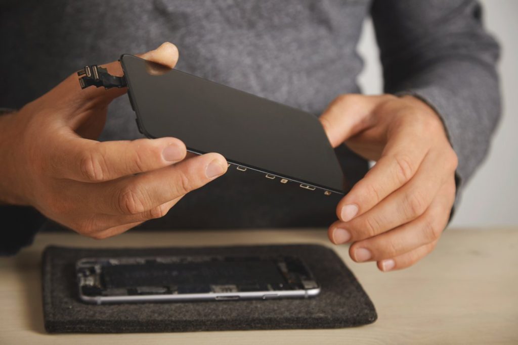 Tekniker løfter iPhone-skærm under skærmskift, hvor Face ID-sensorerne i toppen skal flyttes med